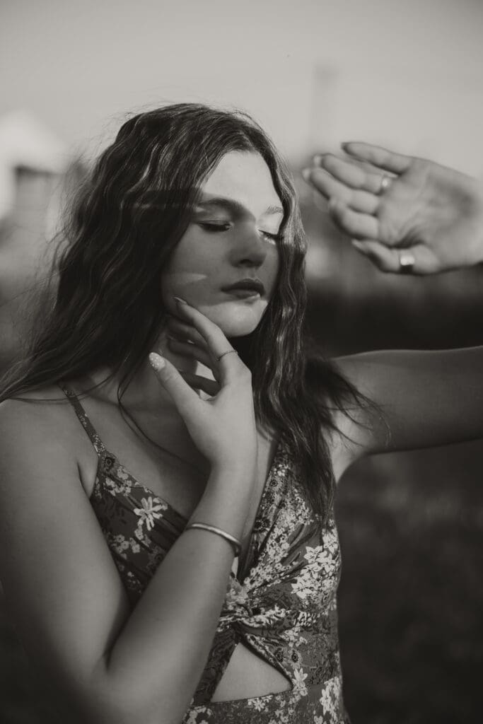 black and white photo of senior girl standing out side with her hand blocking the sun