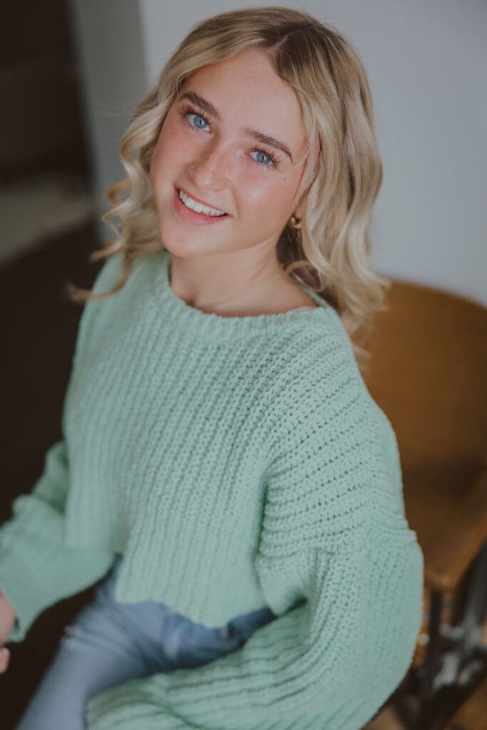 blonde senior girl smiling wearing green sweater and jeans for studio session