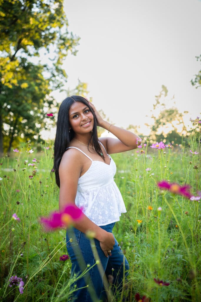 senior girl in jeans and white top standing in flowers