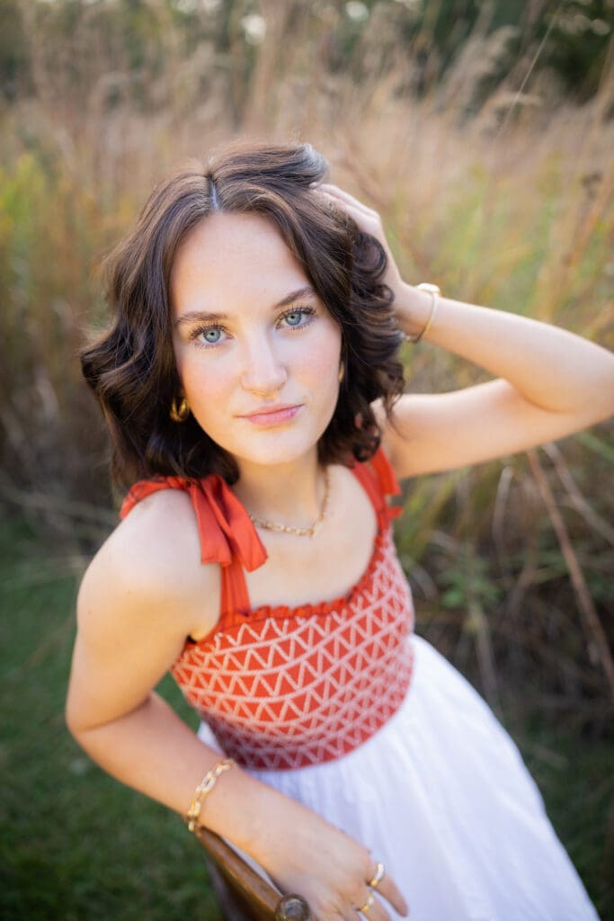 senior girl in orange and white dress sitting on chair in tall grass