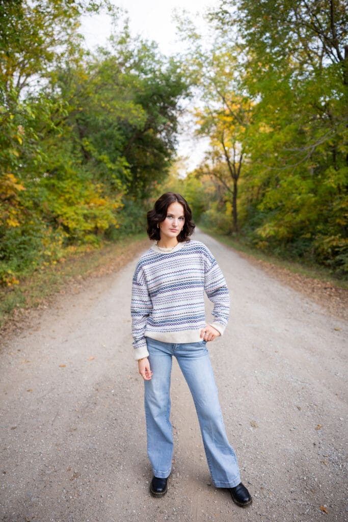 senior girl in sweater and jeans standing in the middle of a gravel road