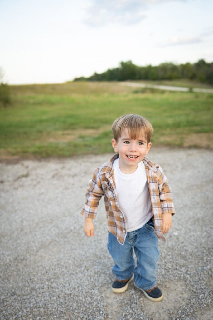 Young boy in overalls smiling at the camera with soft background blur.