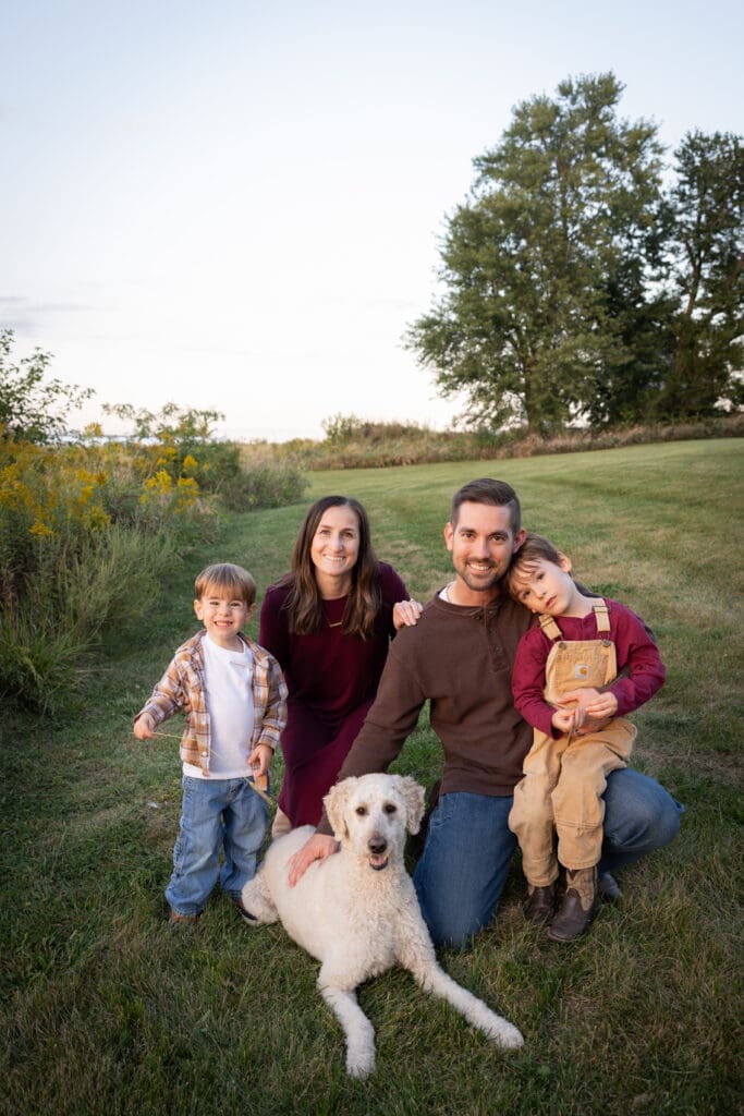 Family sitting together with their dog near a field at sunset.