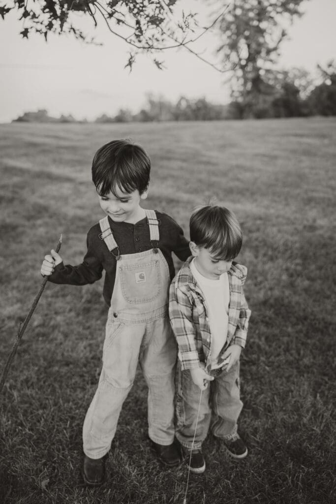 Black and white photo of the two boys standing in the grass holding sticks.