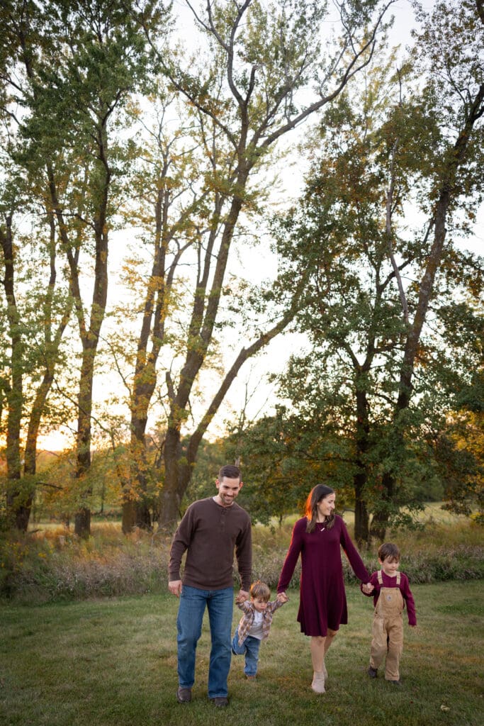 Family holding hands while walking through tall trees at sunset.