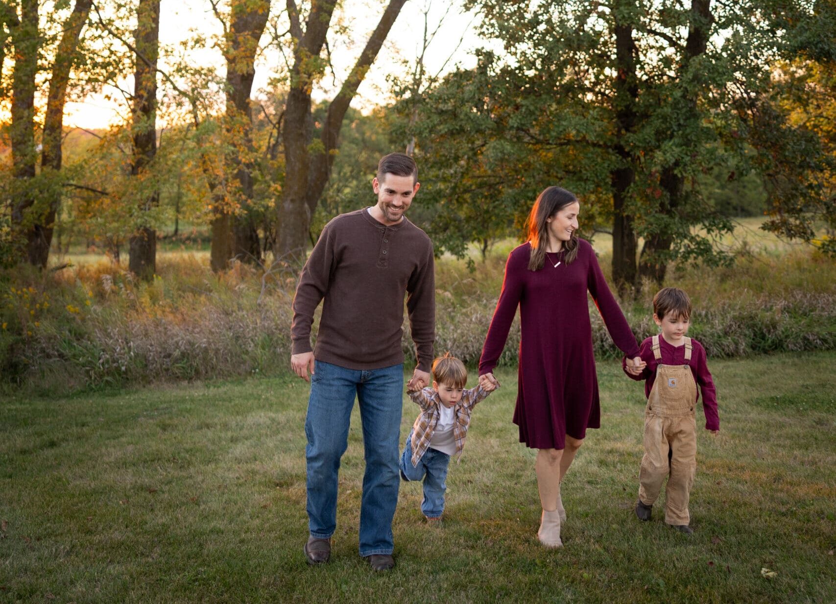 Family holding hands while walking through tall trees at sunset.