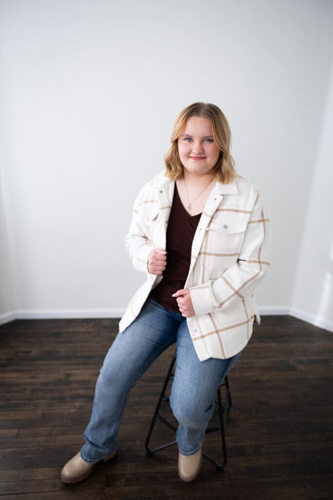 senior girl studio session sitting on stool holding jacket