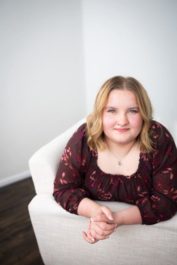senior girl in floral dress leaning on couch for studio photo session