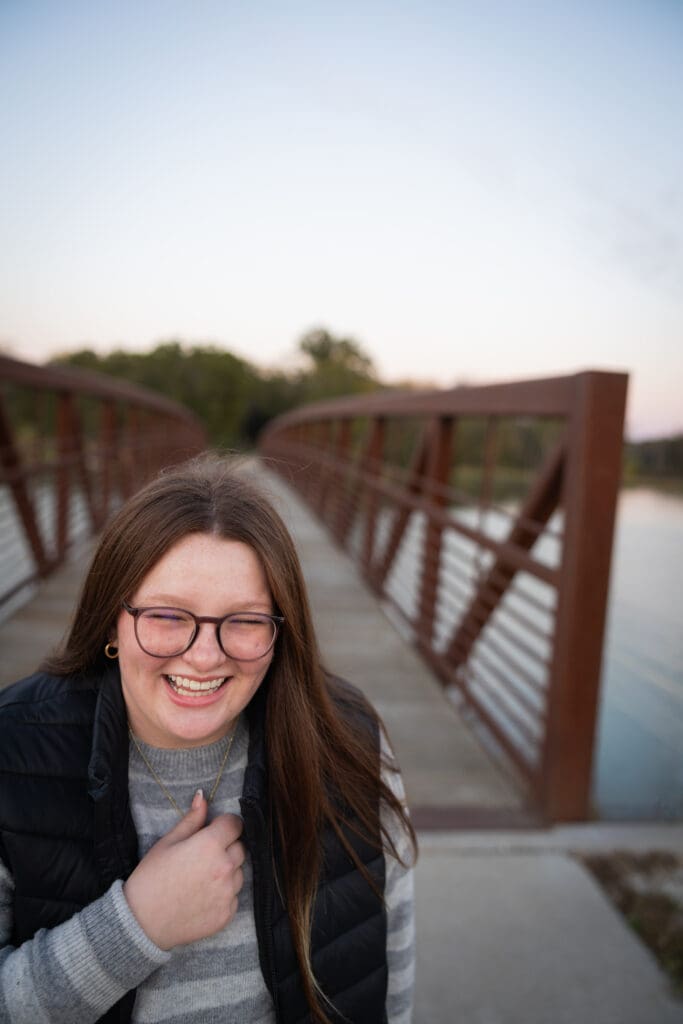 girl laughing outdoor senior photos at lake darling state park bridge in the backgroun