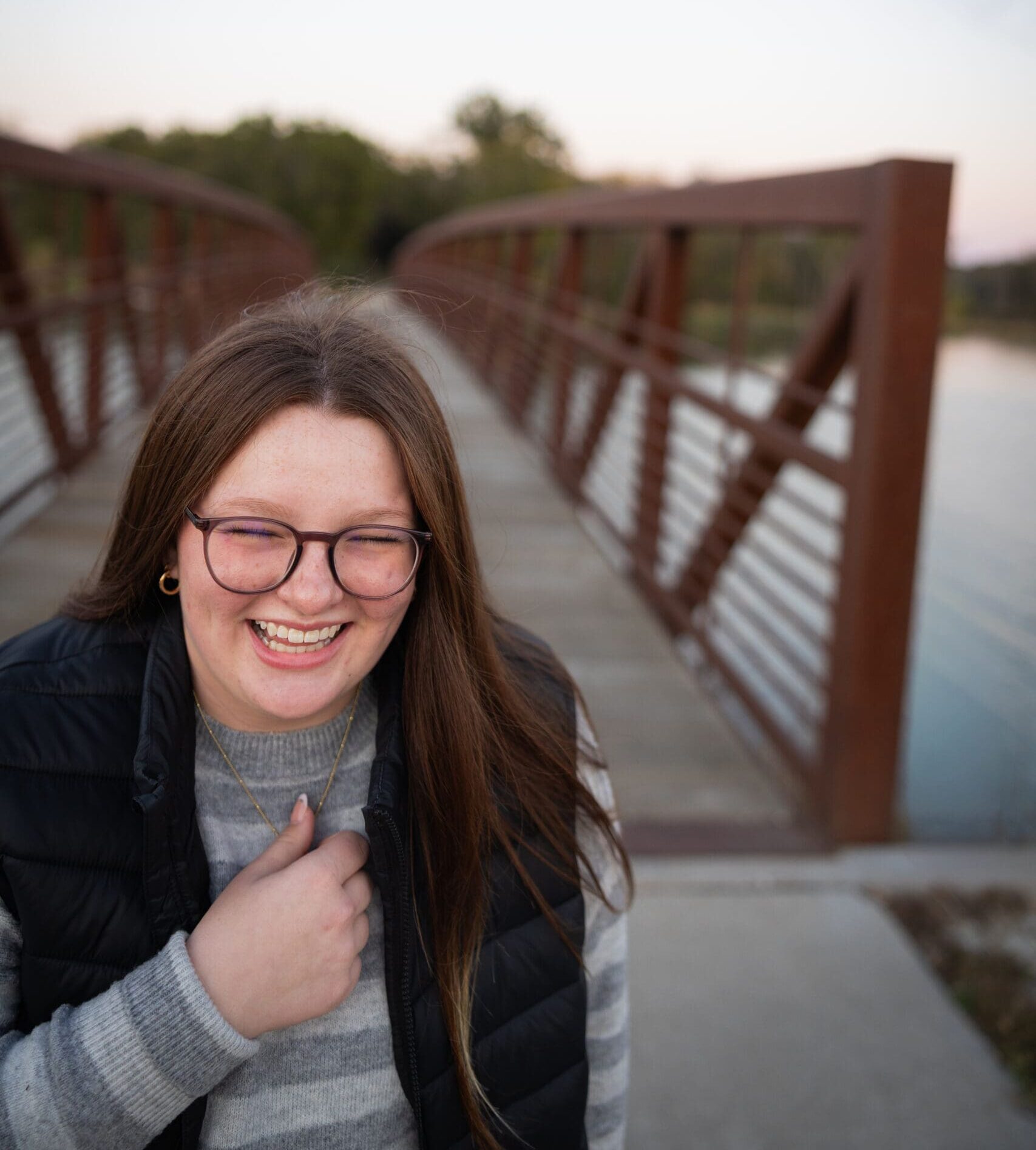 girl laughing outdoor senior photos at lake darling state park bridge in the backgroun