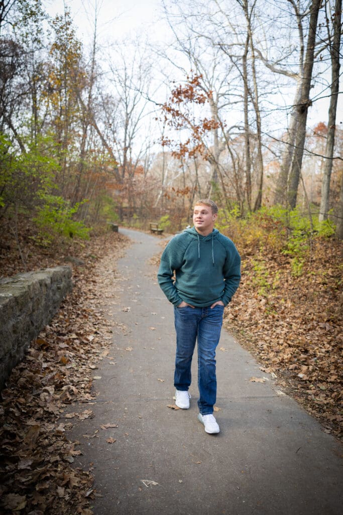 senior guy in hoodie senior photos walking on path at starrs cave burlington iowa