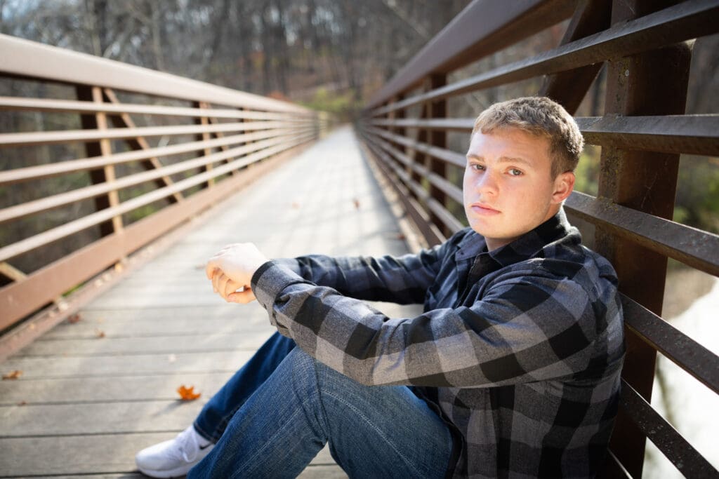 Senior Guy Sitting on bridge for fall photos in plaid shirt