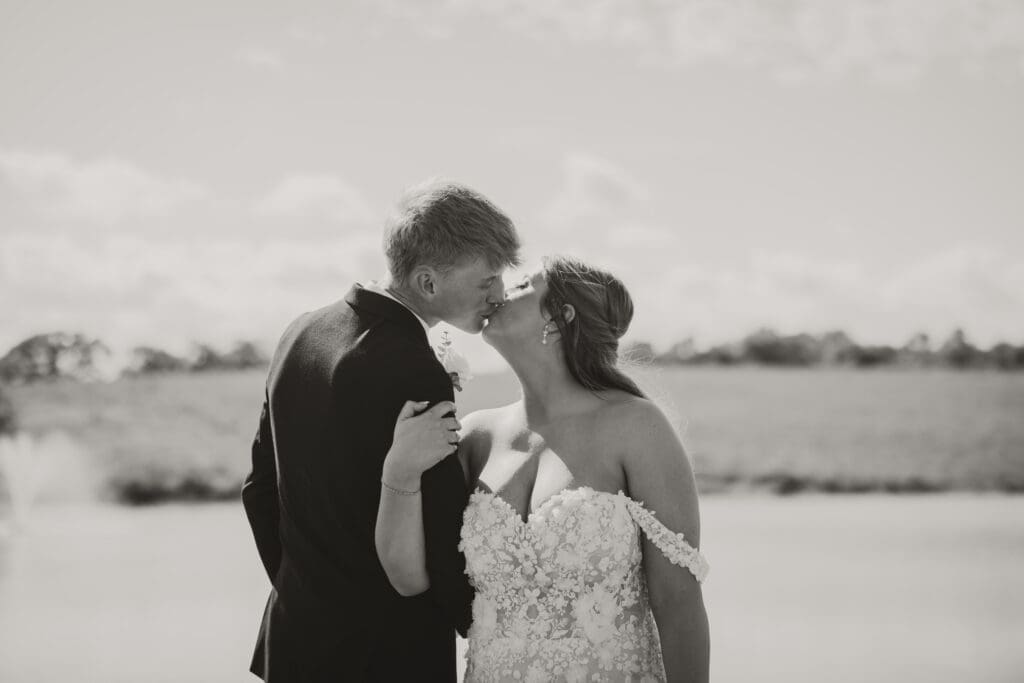 bride and groom kissing in front of pond black and white